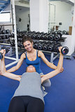 Cheerful female trainer helping woman lifting weights