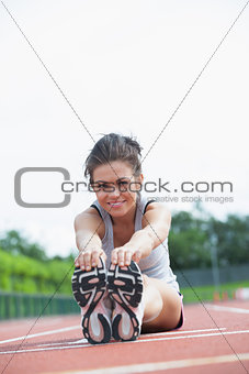 Smiling woman stretching on track