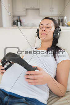 Pregnant woman listening to music and holding headphones on belly