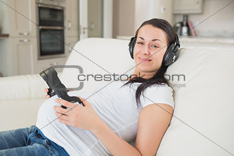 Prospective mother lying on the couch listening to music and holding headphones to belly