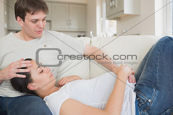 Pregnant woman resting on husband on sofa
