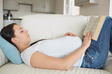 Young pregnant woman reading on sofa