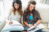 Two women sitting in a couch writing  notepads