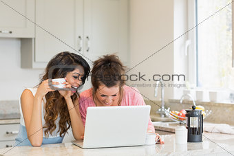 Happy women having coffee while looking at a laptop
