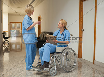 Nurse with drink talking to nurse in wheelchair with folder