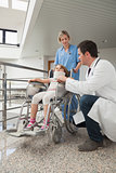 Doctor crouching next to child in wheelchair with nurse pushing it