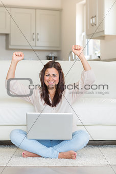 Successful woman raising her hands in front of laptop
