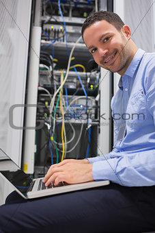 Smiling man using the laptop next to servers