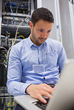 Man working on laptop in front of servers