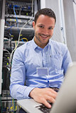 Smiling man working on servers with laptop