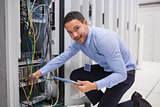 Smiling technician with tablet pc plugging cables into server