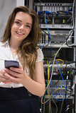 Smiling woman with smartphone in front of servers