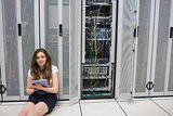 Smiling woman sitting on floor checking servers with tablet pc