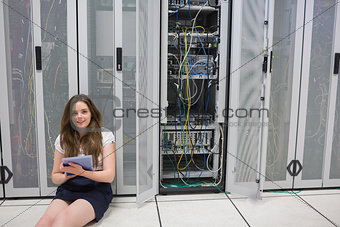 Smiling woman sitting on floor checking servers with tablet pc