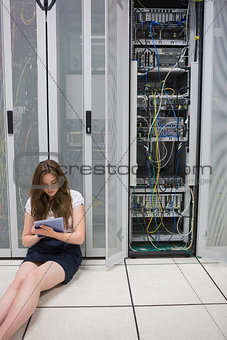 Woman working on servers with tablet pc sitting on floor