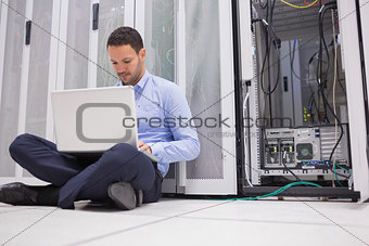 Man sitting on floor with laptop beside servers