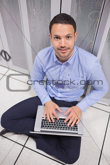 Smiling man using laptop in front of servers