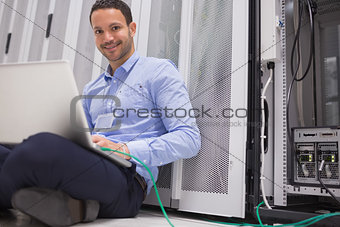 Happy technician working on laptop connected to server