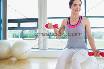 Happy woman lifting weights on exercise ball