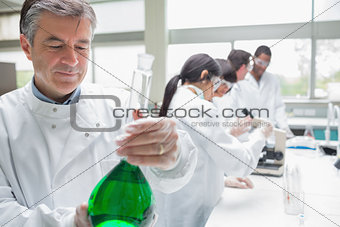 Chemist viewing liquid while other persons doing research