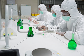 Chemists testing green liquid in petri dishes