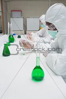 Chemists in protective suits working with green chemical