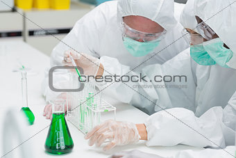 Two chemists adding green liquid to test tubes