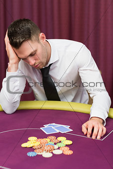 Man leaning on poker table looking disappointed