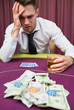 Man drinking whiskey looking stressed at poker table