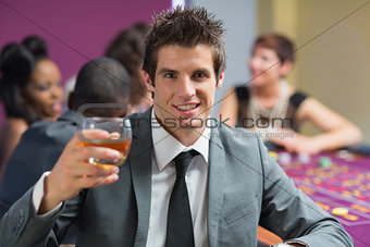 Man raising whiskey glass at roulette table