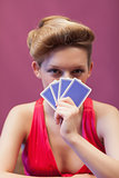 Woman in a casino holding cards before face