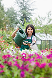 Cheerful woman working in garden center watering the plants