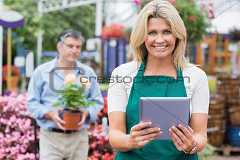 Smiling woman holding a tablet pc with customer holding plant behind