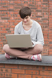 Man sitting cross legged and using laptop outside