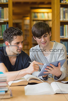 Student showing another something on tablet in library