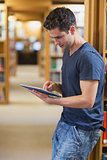 Man leaning against book shelf using tablet pc