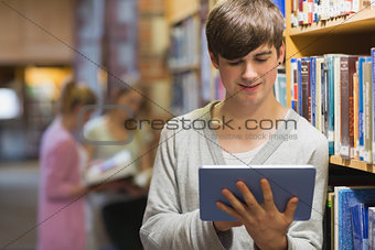 Man leaning at a bookshelf holding a tablet pc