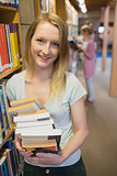 Student standing at a bookshelf at the library holding books