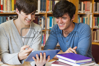 Students sitting at library desk looking at tablet pc