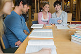 Students sitting at library table smiling while holding a tablet pc