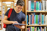 Student leaning against bookshelf holding a tablet pc