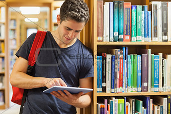 Student leaning against bookshelf holding a tablet pc