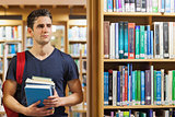 Student standing at the library holding pile of books