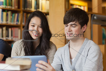 Students sitting at the library holding a tablet pc
