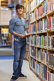 Student standing at a bookshelf smiling holding a tablet pc