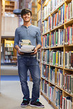Man standing at a bookshelf holding a pile of books