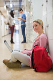 Woman sitting on the floor holding a laptop in college hallway