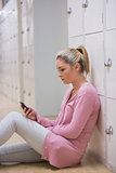 Woman sitting against locker texting