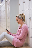 Smiling woman sitting against lockers texting