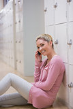 Woman sitting on the floor against lockers phoning while smiling